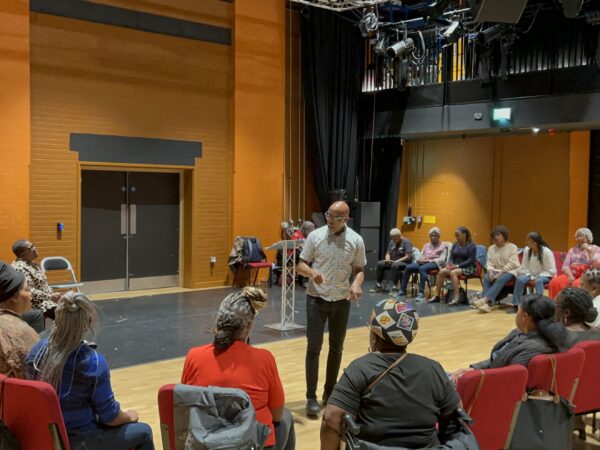 Singers sat in a circle being led by Colin Anderson as part of the Caribbean Folk Song Workshop