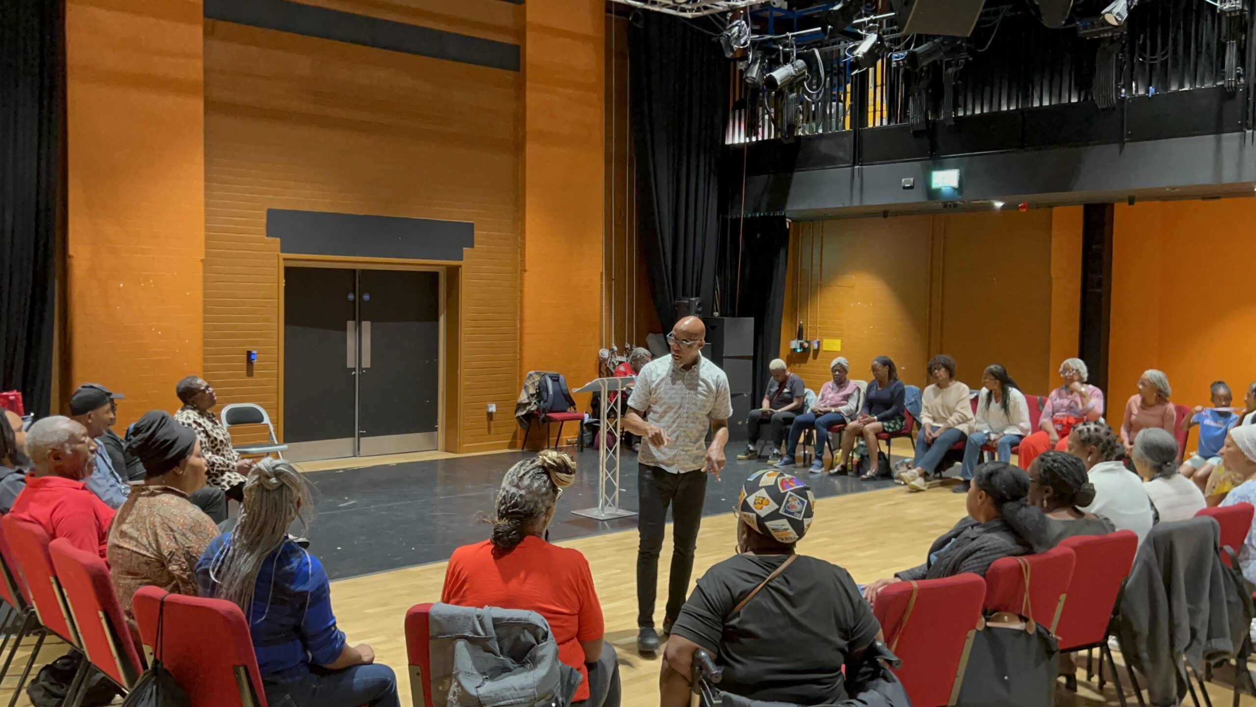 Singers sat in a circle being led by Colin Anderson as part of the Caribbean Folk Song Workshop